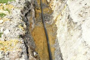 A plastic black gas pipe at the bottom of the trench. A dug trench for laying a gas pipe. photo