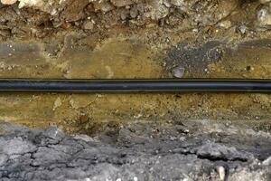 A plastic black gas pipe at the bottom of the trench. A dug trench for laying a gas pipe. photo