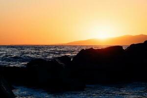 puesta de sol detrás el rocas en el playa foto