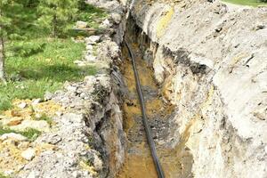 A plastic black gas pipe at the bottom of the trench. A dug trench for laying a gas pipe. photo