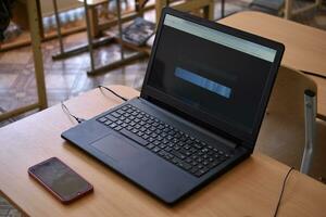 un negro ordenador portátil y un teléfono en el escritorio. un oficina lugar de trabajo con un computadora. foto