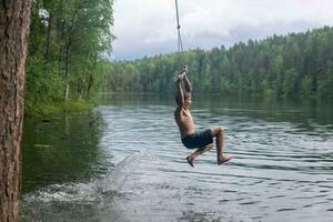 boy jumps into the water using a tarzan swing while swimming in a forest lake photo