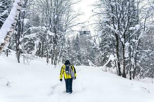 mochilero camina a lo largo un camino en un invierno bosque, siguiendo un quadcopter foto