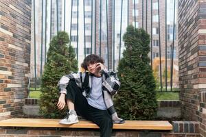 young man talking on the phone while sitting on a bench in the city photo