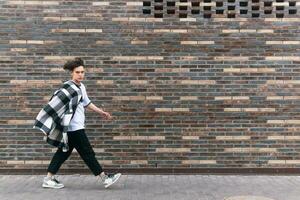 young man walks down the street in front of a brick wall photo