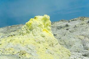 cone of sulfur deposits around a fumarole in a solfataric field against a blue sky photo