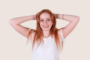 smiling redhead young woman with tousled hair stretches on a light background photo