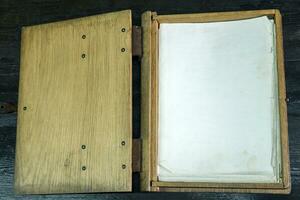 old log book in a wooden case with clasps on a black tabletop, open photo