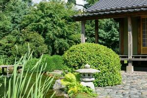 Roca linterna en el apuntalar de un estanque en un japonés jardín con un té casa foto