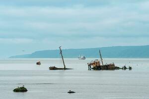 remains of a sunken ship against the backdrop of a sea bay with foggy mountains in the background photo