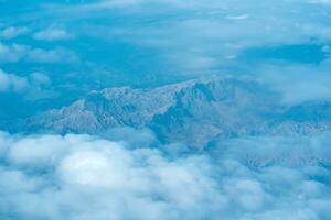 view of the earth below while flying above the clouds, mountainous terrain through atmospheric haze, view from above photo