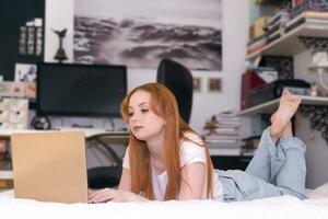 young woman lying with laptop on bed at home photo