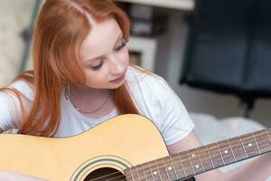 young woman playing acoustic guitar at home, portrait close-up photo