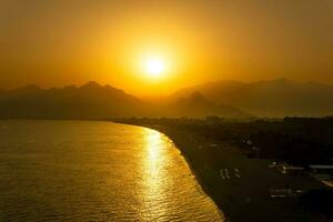 sunset view of Konyaalti beach from nearby rocks in Antalya, Turkey. Beydaglari mountains in fog are visible in the background. photo