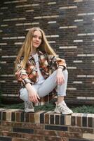 young woman sitting near brick wall of city building photo