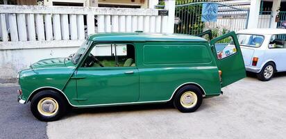 Bangkok, Thailand - September 29, 2023 Green with Blue and white classic Mini cooper van parked on street and in front of house. Transportation, Vintage, Old or Retro Vehicle concept. photo