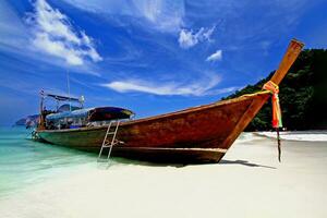 Big long tail boat parking on the white sand beach with blue sky and white clouds at Phi Phi island Krabi, Thailand. photo