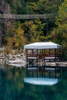 autumn mountain landscape with shady lake, picnic gazebo and hanging bridge photo