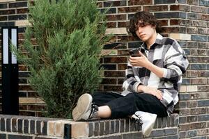 young man reads something on the phone while sitting on the brick curb photo