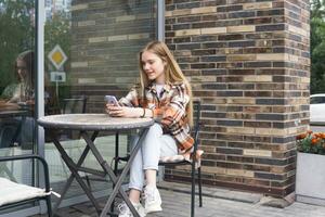 young woman reading funny message on phone while sitting at an outdoor cafeteria table photo