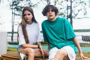 two young people are sitting on a bench in a coastal park photo