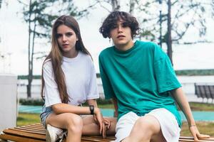 two young people are sitting on a bench in a coastal park photo