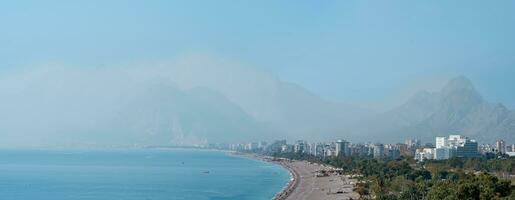 view of Konyaalti beach from nearby rocks in Antalya, Turkey. Beydaglari mountains in fog are visible in the background. photo