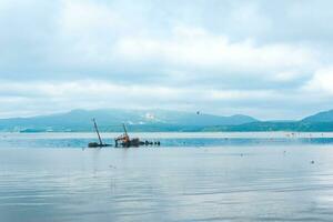 sunken ship against the backdrop of a sea bay with foggy mountains in the background photo