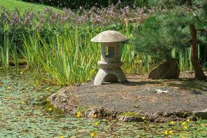 Roca linterna en un pequeño isla en el medio de un estanque en un japonés jardín foto