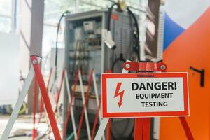 sign with the inscription Danger Equipment testing on the fence against the background of blurred electrical facilities in the workshop photo
