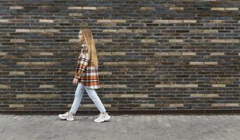 young woman walks down the street in front of a brick wall photo