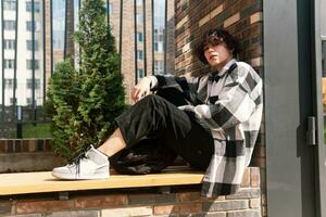 young man sits relaxed on a city bench photo