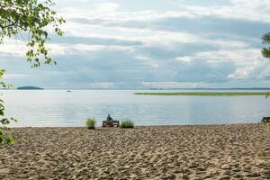 sandy beach on the shore of a vast lake, a woman traveler is sitting on a bench made of old pallets photo