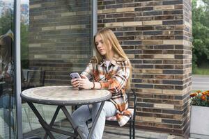 young woman typing something on the phone while sitting at an outdoor cafeteria table photo