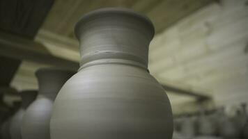 Close up of set of clay ceramic jugs and lids while drying. Stock footage. Row of hand made clay pots standing in hot wooden room, ceramics and manufacture concept. photo