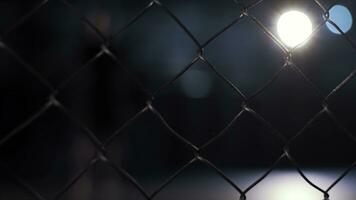 Close up of chain link fence on dark blurred background with shining lamp. Video. Metal lattice inside the building, grunge style. photo