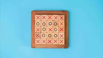 Wooden game board tic-tac-toe. Turning of the letters X-O and middle one different from each other on blue background. video