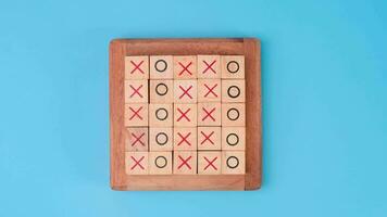 Wooden game board tic-tac-toe. Turning of the letters X-O and middle one different from each other on blue background. video