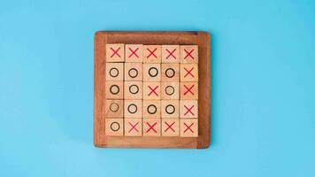 Wooden game board tic-tac-toe. Turning of the letters X-O and middle one different from each other on blue background. video