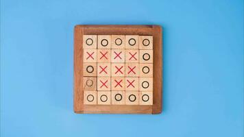 Wooden game board tic-tac-toe. Turning of the letters X-O and middle one different from each other on blue background. video