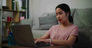 Footage of Young woman sitting on the floor leaning against a sofa working with a laptop and typing work at home office. video