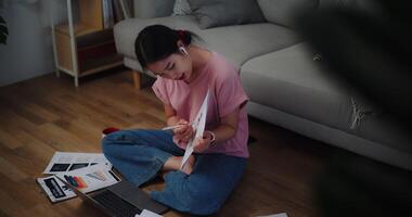 beeldmateriaal van jong vrouw zittend Aan de verdieping Holding documenten video telefoontje presentatie Aan laptop Bij huis kantoor.