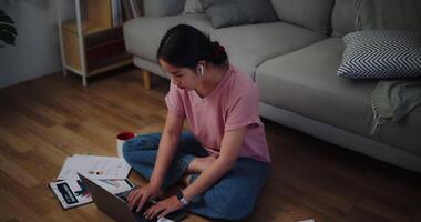 metraggio di giovane donna seduta su il pavimento Lavorando con un' il computer portatile e controllo carta da lavoro a casa ufficio. video