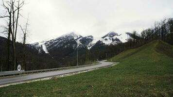 Lonely car on a mountain road turn on snowy peaks and cloudy heavy sky background. Stock footage. Mountain road car trip view. photo