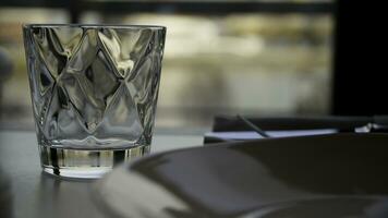 Faceted glass of water on nature background. Clear faceted glass with whiskey on a dark wooden table, close-up. Empty faceted glass photo