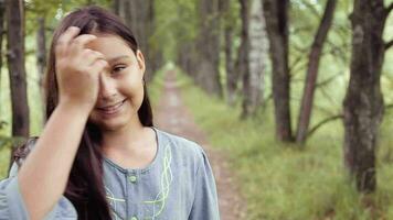 portret. een mooi hoor mooi weinig meisje met lang zwart haar- glimlacht heel prachtig in de camera terwijl poseren staand Aan natuur in een zomer zonnig dag video