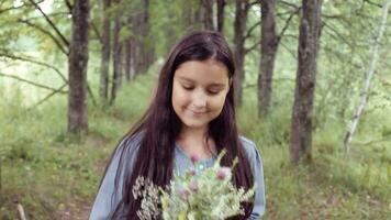 portret. een weinig mooi meisje met lang haar- wandelingen Aan natuur in de zonnig dag Holding een boeket van bloemen in haar handen en looks Bij het hebben een mooi hoor glimlach en hebben een mooi zo humeur. langzaam beweging video