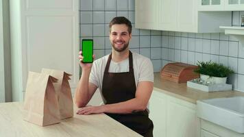 végétalien cuisson, Masculin chef, en bonne santé alimentaire, nourriture livraison. une homme détient une téléphone intelligent avec une vert écran dans le sien main et sourit tandis que séance dans le cuisine. Accueil livraison app video