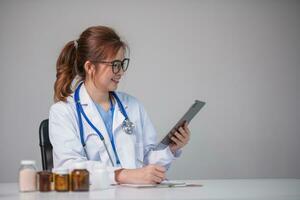 Young Asian doctor in a white medical uniform with a stethoscope using a lab computer and tablet to organize and classify medicines in preparation for administration to patients. photo