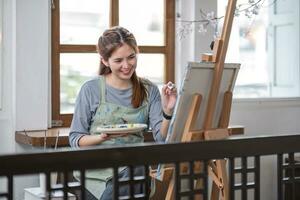 Young female artist works on abstract acrylic painting on canvas in art painting studio. photo